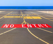 no entry sign at the runway of the airport with ocean in backgro