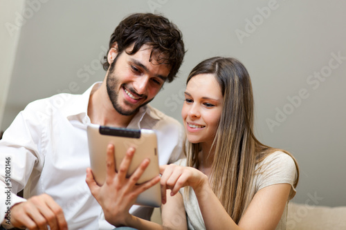 Photo: Couple sitting on sofa with electronic tablet Couple sitting on sofa with electronic tablet