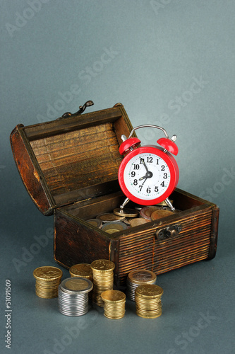 Photo: Alarm clock with coins in chest on grey background Alarm clock with coins in chest on grey background