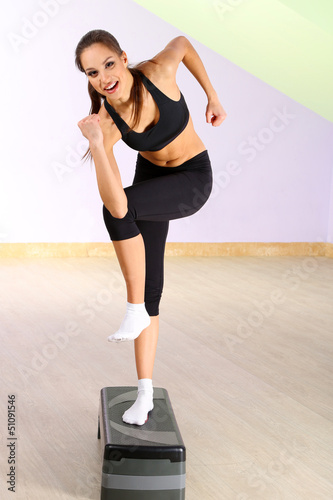 Photo: Young woman doing fitness exercises on stepper at gymnasium Young woman doing fitness exercises on stepper at gymnasium