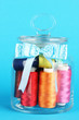 Glass jar containing various colored thread on blue background