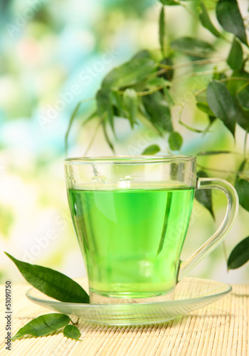 Photo: Transparent cup of green tea on bamboo mat, on nature Transparent cup of green tea on bamboo mat, on nature