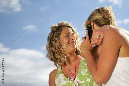 Photo: Two blond friends making a call whilst at the beach Two blond friends making a call whilst at the beach