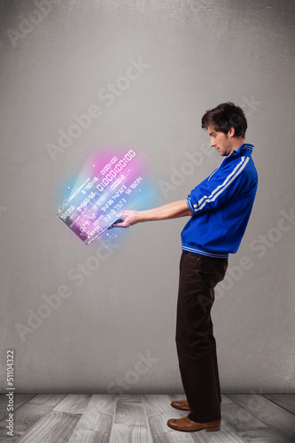Photo: Casual man holding laptop with exploding data and numbers Casual man holding laptop with exploding data and numbers