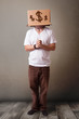 Young man gesturing with a cardboard box on his head with dollar