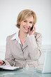 Businesswoman sat at desk holding mobile telephone