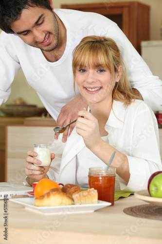 Photo: Woman eating breakfast while her affectionate boyfriend Woman eating breakfast while her affectionate boyfriend