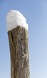 Holzpfahl mit Schnee vor blauem Himmel