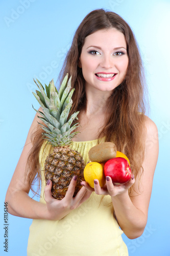 Photo: Beautiful woman with pineapple and fruits on blue background Beautiful woman with pineapple and fruits on blue background
