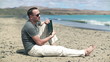 Young man sitting on the beach and chatting with tablet computer