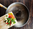 Fresh vegetables on the cutting board are falling in the wok. Co