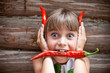 Photo : Girl with a red hot chili pepper in her mouth show devil horns Girl with a red hot chili pepper in her mouth show devil horns