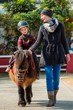 Mother riding her son on a pony wearing protective helmet
