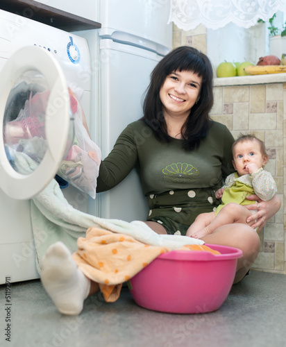 Photo: woman with baby putting clothes in to washing machine woman with baby putting clothes in to washing machine