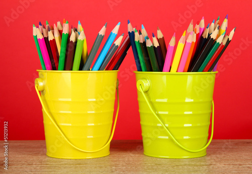 Photo: Colorful pencils in two pails on table on red background Colorful pencils in two pails on table on red background