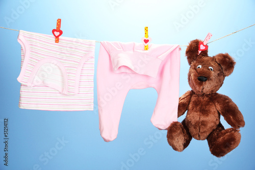 Photo: Baby clothes hanging on clothesline, on color background Baby clothes hanging on clothesline, on color background