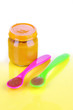 Baby food with weaning spoons on yellow background