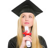 Portrait of thoughtful woman in graduation gown with diploma