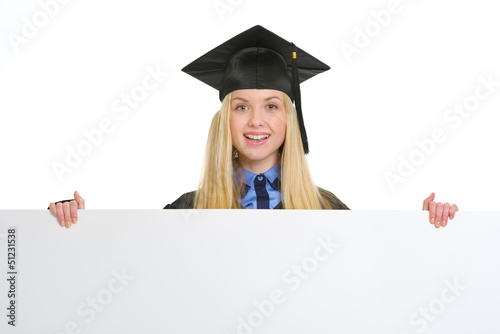 Photo: Smiling young woman in graduation gown showing blank billboard Smiling young woman in graduation gown showing blank billboard