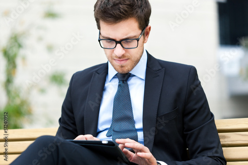 Photo: Young businessman using a tablet on a bench in the city Young businessman using a tablet on a bench in the city