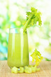 Glass of celery juice, on bamboo mat, on green background
