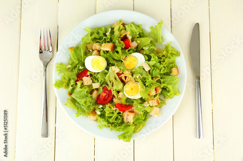 Photo: Caesar salad on white plate, on color wooden background Caesar salad on white plate, on color wooden background