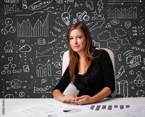 Photo: Businesswoman sitting at desk with business scheme and icons Businesswoman sitting at desk with business scheme and icons