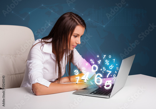 Photo: Beautiful young woman sitting at desk and typing on laptop with Beautiful young woman sitting at desk and typing on laptop with