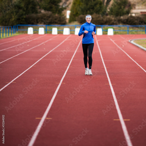 Photo: Young woman running at a track and field stadium Young woman running at a track and field stadium