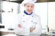 male chef smiling while standing in restaurant kitchen