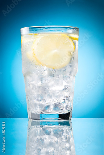 Photo: Water glass with lemon and ice isolated on a blue background Water glass with lemon and ice isolated on a blue background