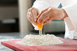 A baker cracking an egg into a pile of flour.