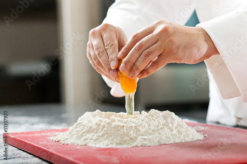 Photo: A baker cracking an egg into a pile of flour. A baker cracking an egg into a pile of flour.