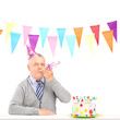 A happy mature man with party hat blowing and a birthday cake