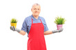 Foto: A mature male gardener with apron holding two potted plants A mature male gardener with apron holding two potted plants