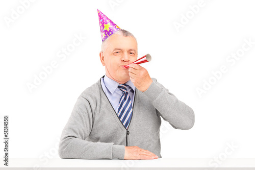 Photo: Mature man with party hat blowing Mature man with party hat blowing