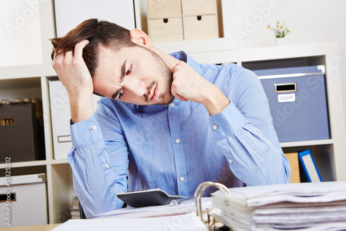 Photo: Nachdenklicher Mann im Büro mit Taschenrechner Nachdenklicher Mann im Büro mit Taschenrechner