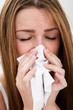Close-up Of A Young Woman Sneezing In To Tissue