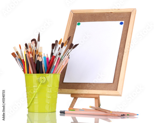Photo: Small easel with sheet of paper with art supplies isolated Small easel with sheet of paper with art supplies isolated