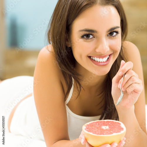 Photo: Portarit of young woman eating grapefruit at home Portarit of young woman eating grapefruit at home
