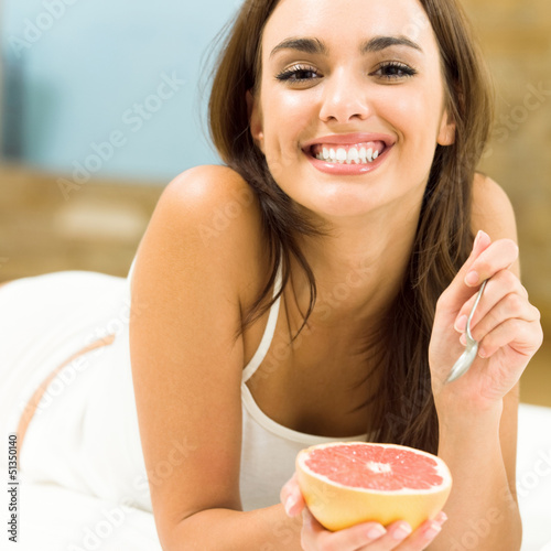 Photo: Portarit of young woman eating grapefruit at home Portarit of young woman eating grapefruit at home