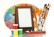 Photo frame as easel with artist's tools isolated on white