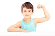 A child showing his muscles seated on a table