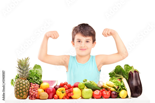 Photo: Healthy child showing his muscles and sitting on a table full of Healthy child showing his muscles and sitting on a table full of