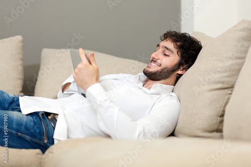 Photo: Portrait of young man relaxing in sofa with electronic tablet Portrait of young man relaxing in sofa with electronic tablet