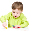 Little boy is drawing on white paper using crayon