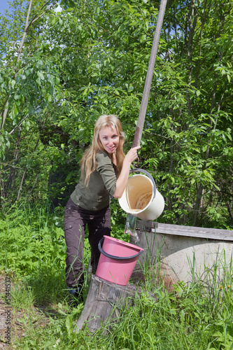 Photo: The young woman at a well, pours water in a bucket.. The young woman at a well, pours water in a bucket..