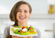 Smiling young woman showing fresh salad