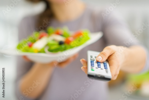 Photo: Closeup on tv remote control and salad in hand of young woman Closeup on tv remote control and salad in hand of young woman