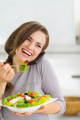 Photo: Smiling young woman eating salad and talking mobile phone Smiling young woman eating salad and talking mobile phone